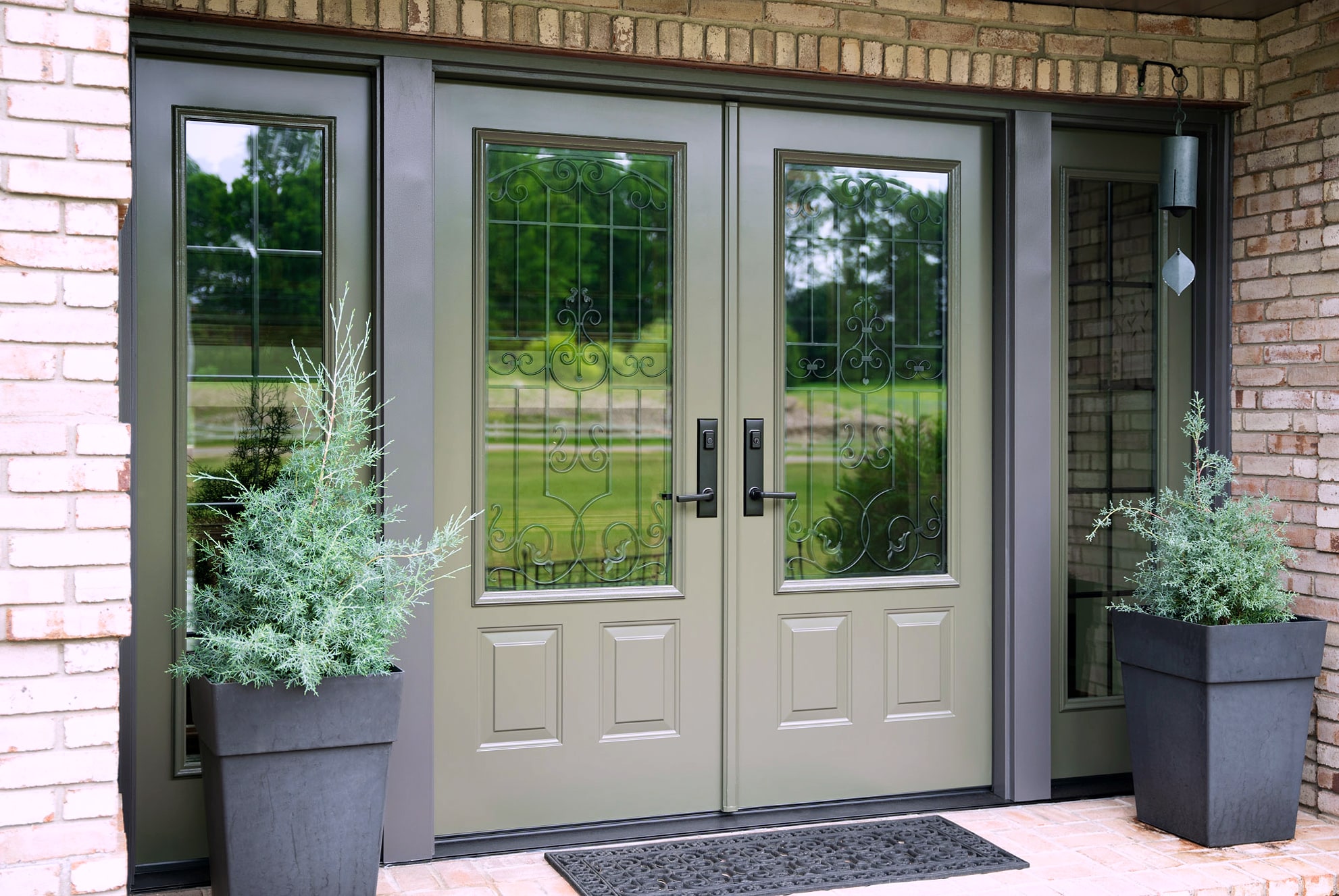 Sage green double entry doors with decorative glass on brick porch